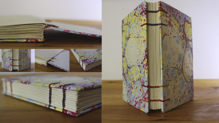 Caderno com costura copta e capa marmorizada colorida, mostrando o cruzamento da linha na lombada