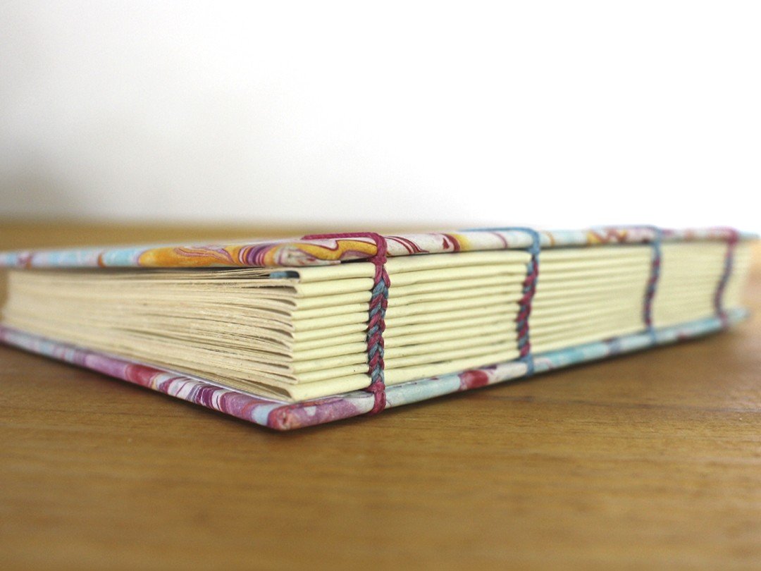 Close da lombada de um caderno com costura copta e capa marmorizada